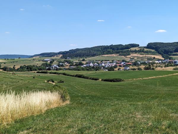 Views of a village nestled in between rolling green fields underneath a bright blue sky.