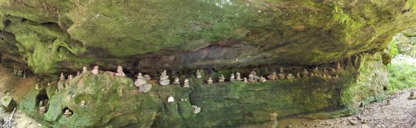 A rock overhang with many small rock cairns set up on a long ledge underneath the overhang.