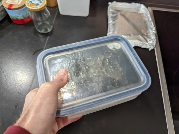 The baking dish with the plastic lid on top being held and shaken. There is liquid sloshing along the inside of the lid.