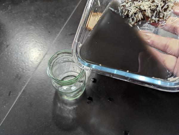 A shot of the black liquid being poured from the baking dish into the small glass jar.