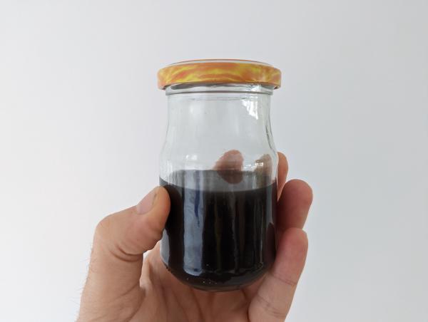 The glass jar roughly half full of the black liquid being held up to a white background.