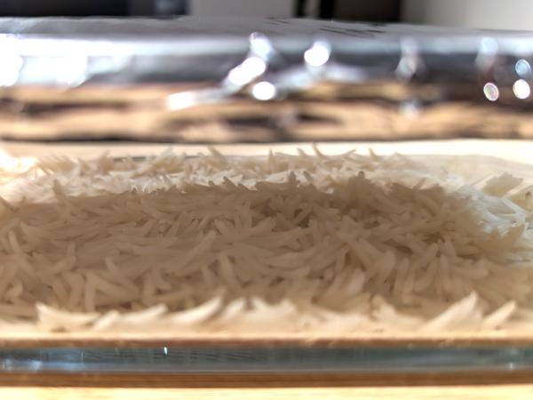 A close up photo through the side of the glass baking dish showing a thin layer of cooked white rice.