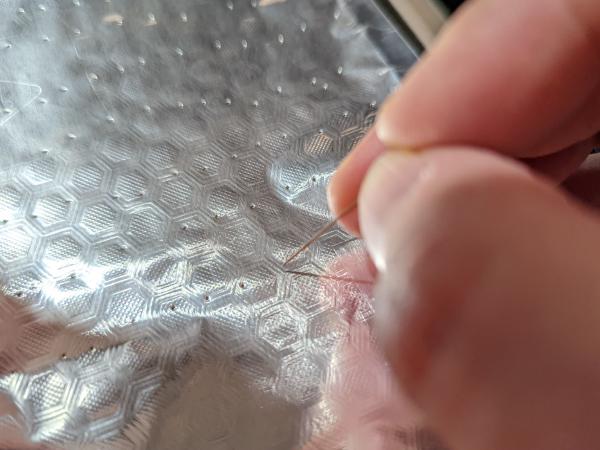 A close up photo of aluminium foil with many tiny holes in it and the pin used to create the holes.