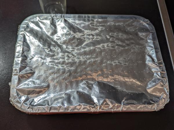 A view of the whole aluminium foil lid with many small holes in it.