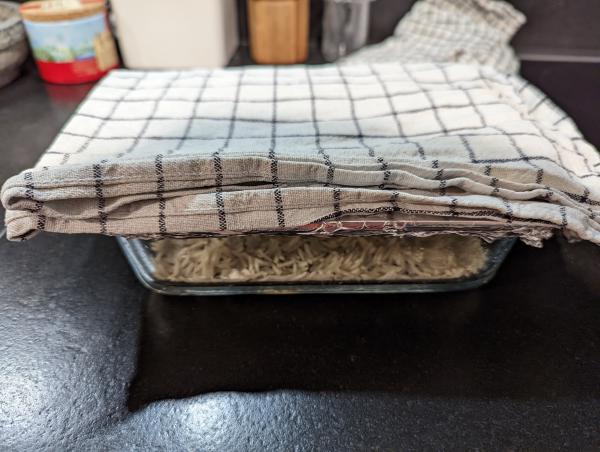 A photo of the covered baking dish sitting on a countertop with a checkered cloth resting on top.
