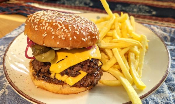 A double cheeseburger with pickled cucumber and red onion sitting on a plate next to a pile of fries.