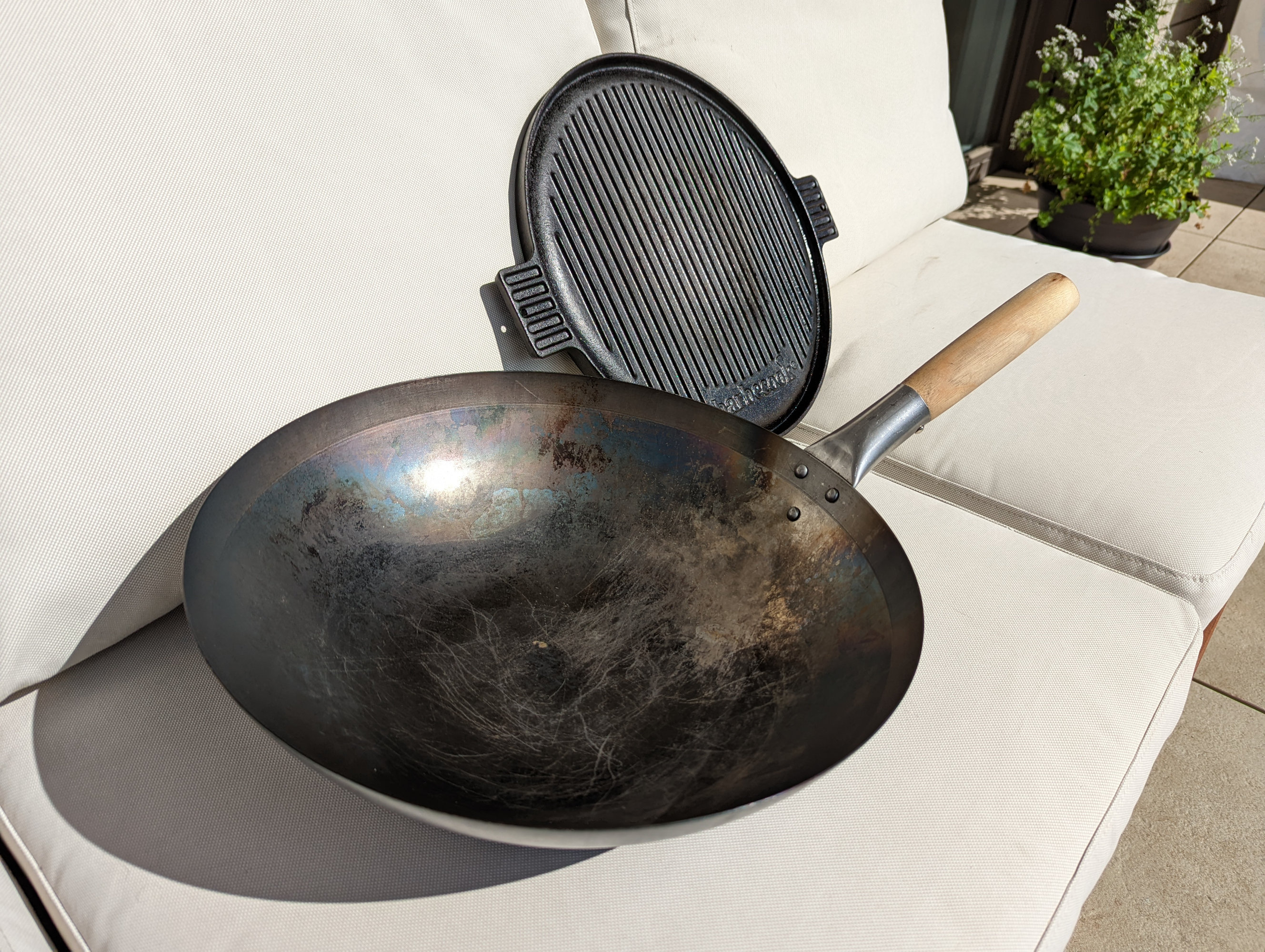 A photo of a wok with a single wooden handle and a round plancha resting next to each other.