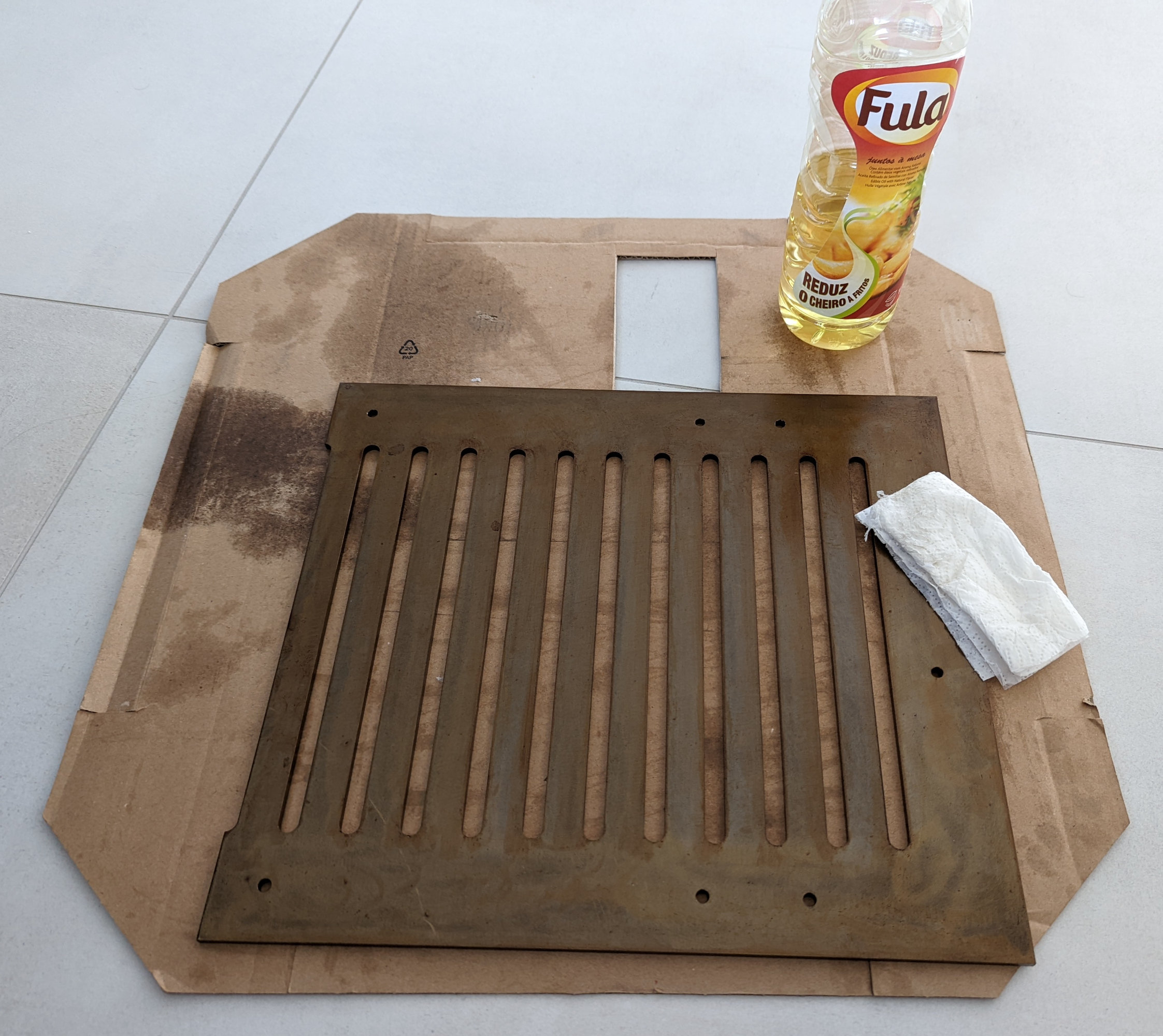 A steel grate sitting on a protective cardboard sheet with an oil soaked paper towel on top.