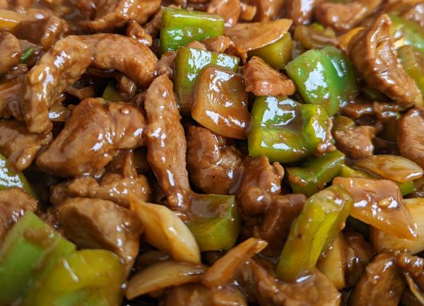 A close up of a mongolian lamb stir fry showing glistening meat, peppers and onion.
